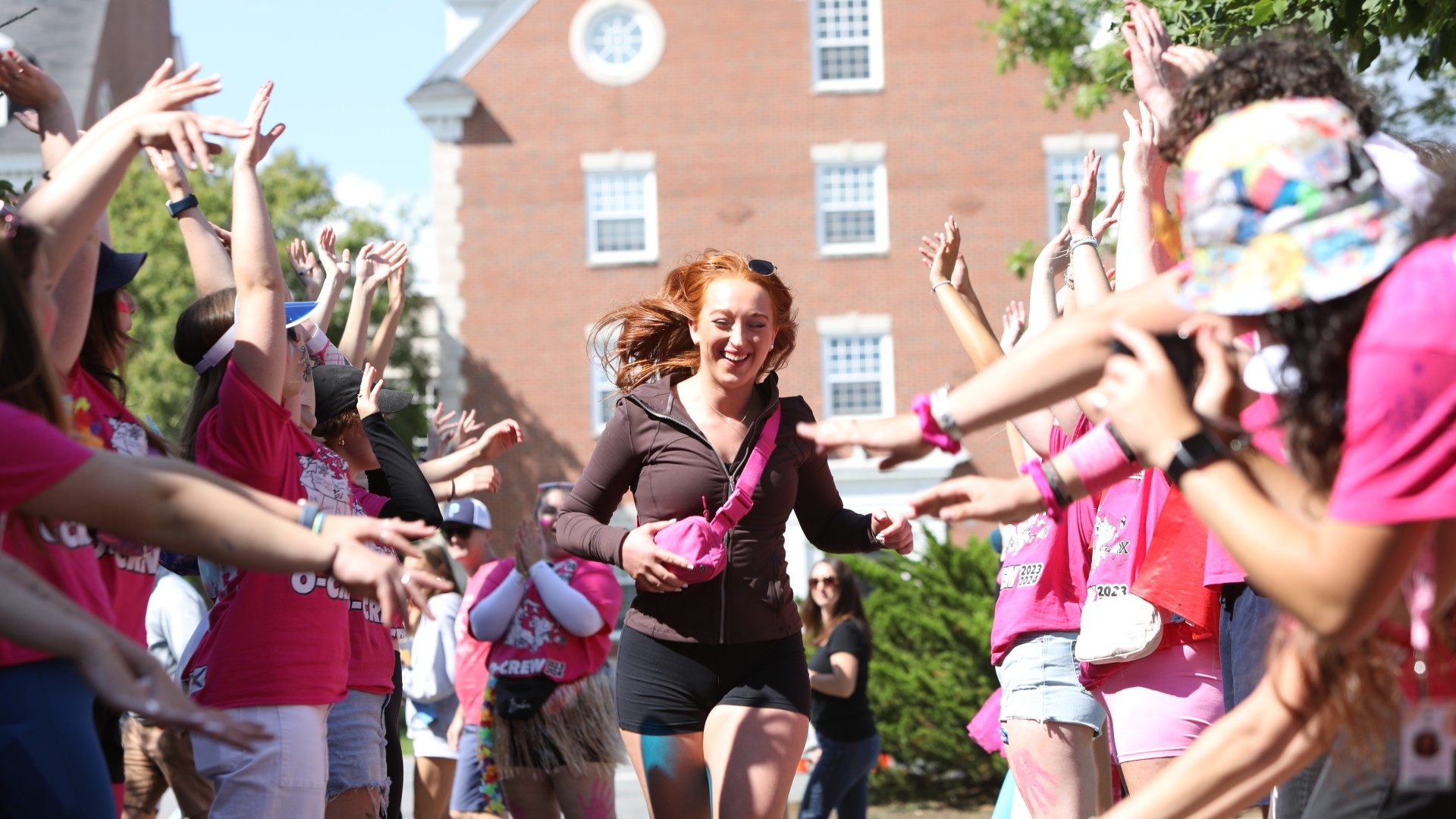 A happy student runs between two lines of cheering people in pink shirts