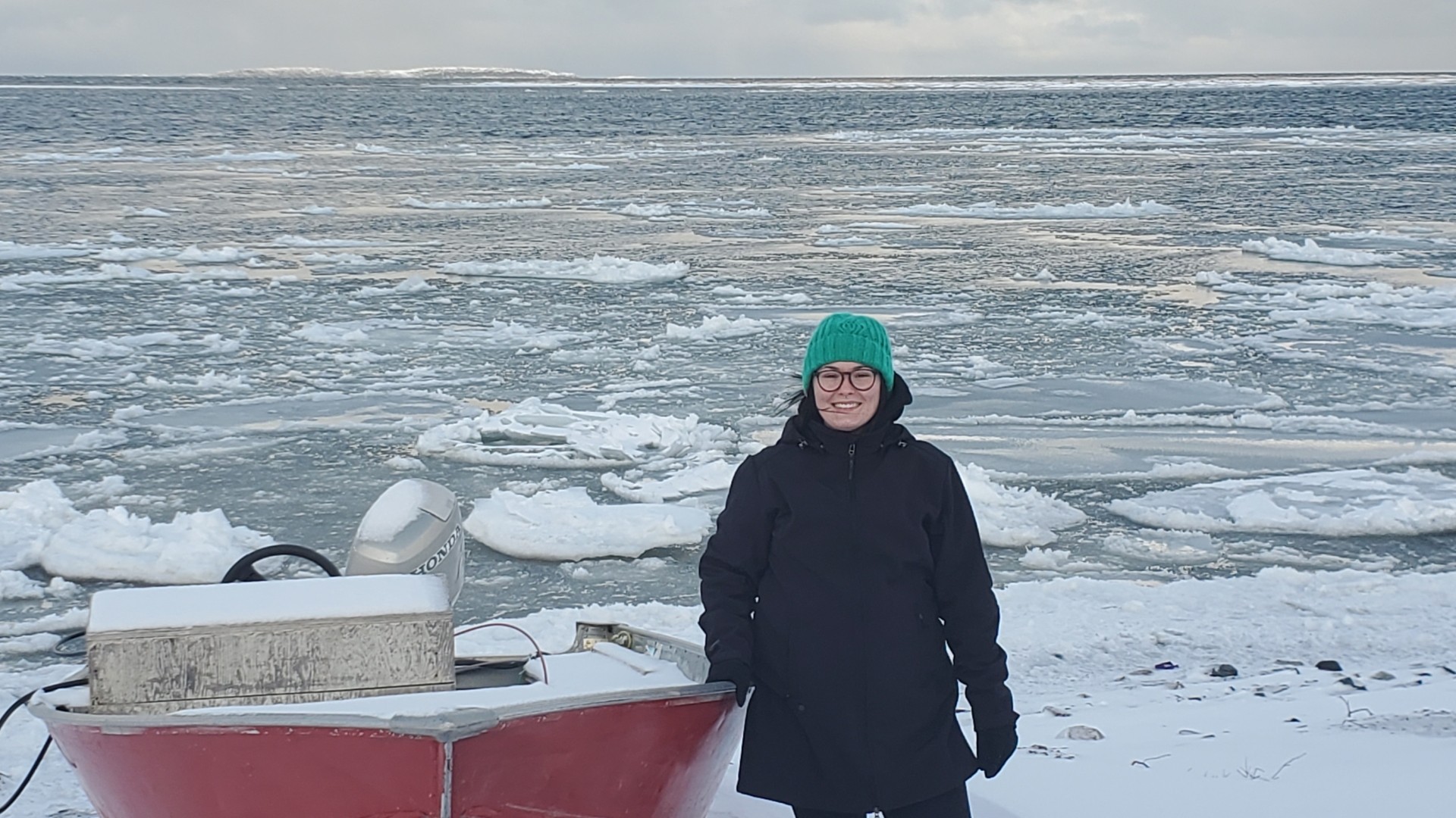 A student standing next to a boat at the edge of icy ocean water