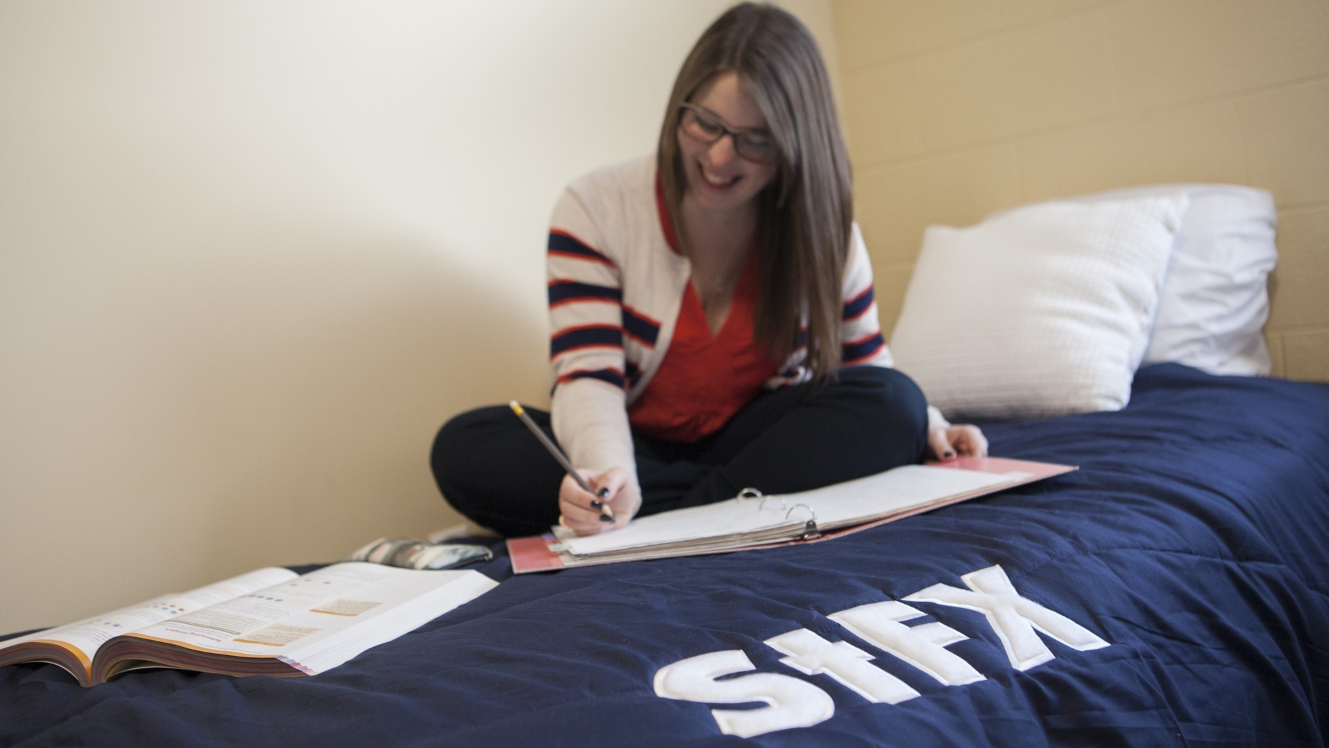 Student studying while sitting on their bed with a StFX comforter.