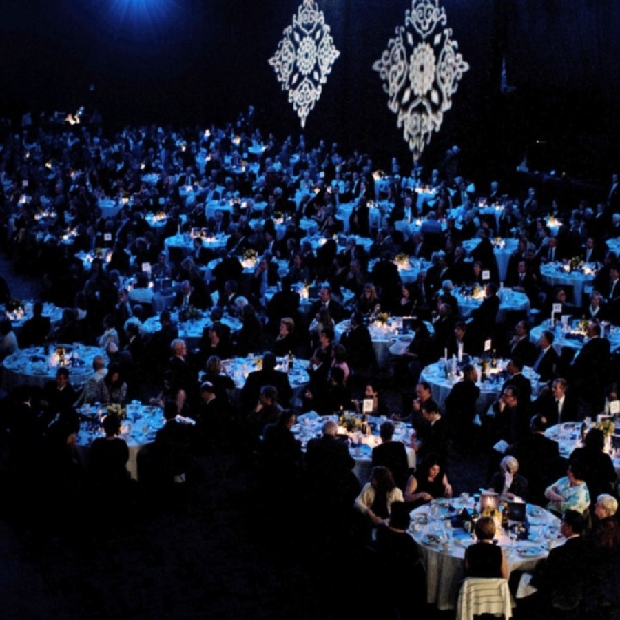 Dark banquet hall with hundreds of guests sitting at round tables