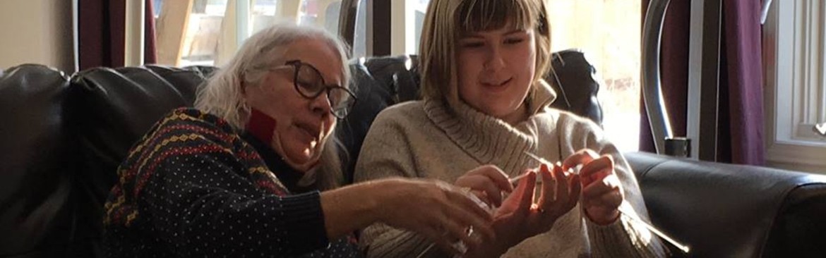 Two people sitting on couch knitting