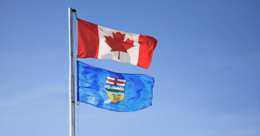The Canadian flag and Alberta provincial flag on the same flagpole against a blue sky.