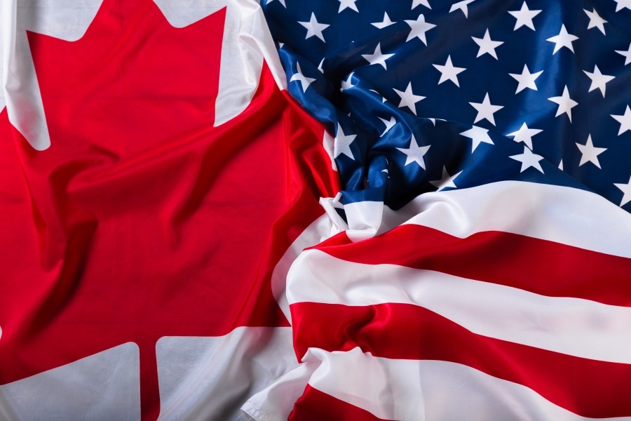 The Canadian flag, which is a red maple leaf on a white background, and the US flag, which is a blue square with white stars on the top and red and white stripes on the bottom, appear in the frame together.