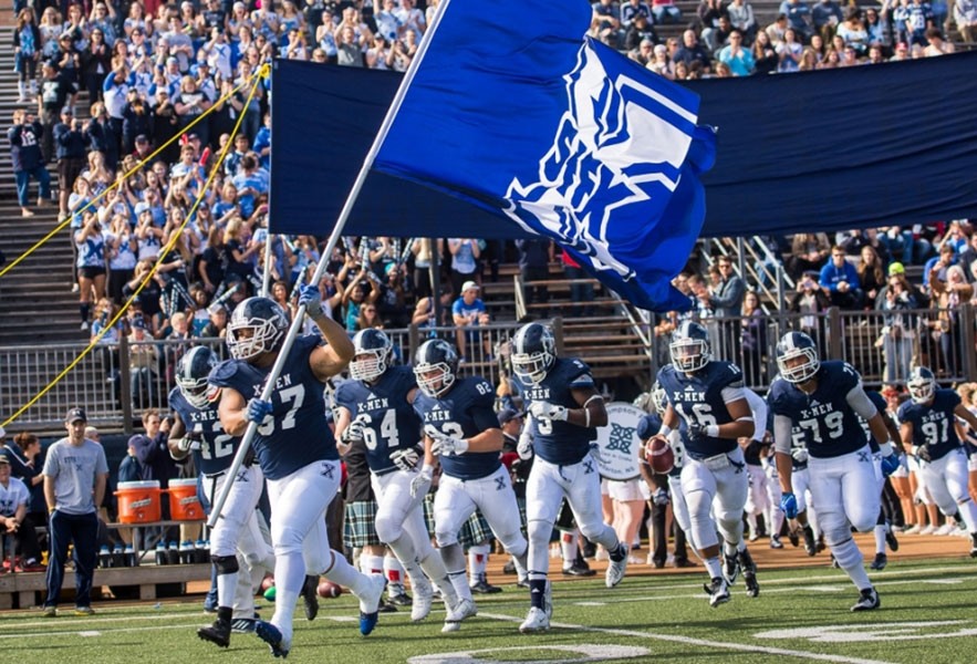 A football team running onto the field with a flag