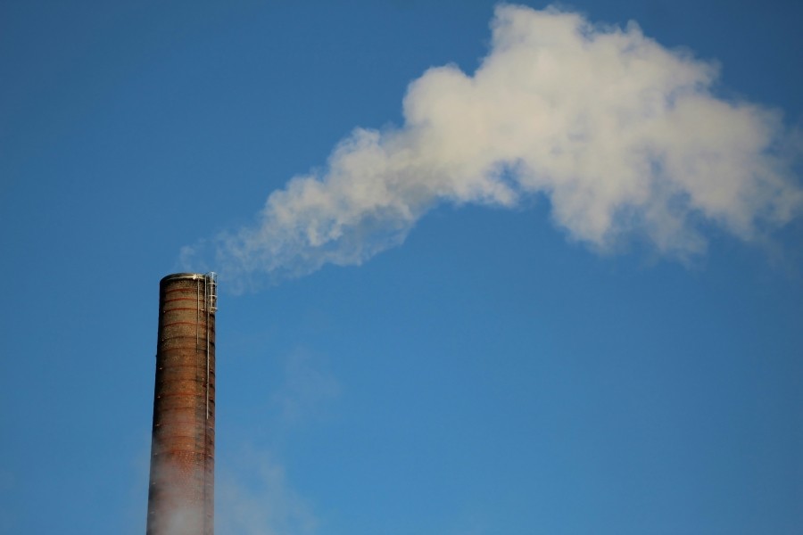 Smoke stack with yellow smoke coming out of the top against a blue sky.
