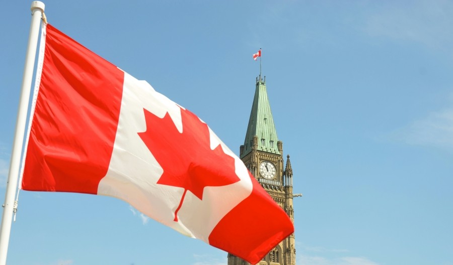 Canadian flag in front of Parliament Hill's Peace Tower against a blue sky..