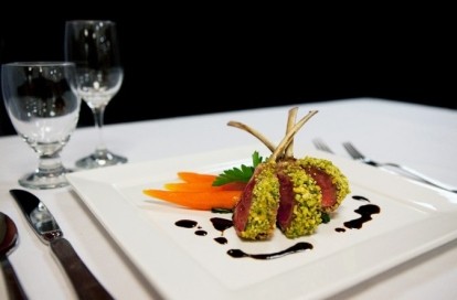 Fancy lamb shanks on square plate with empty wine glasses