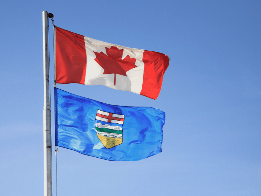 The Canadian flag and Alberta provincial flag on the same flagpole against a blue sky.