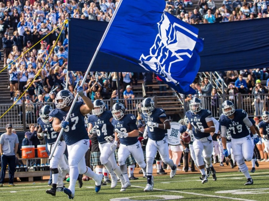 A football team running onto the field with a flag