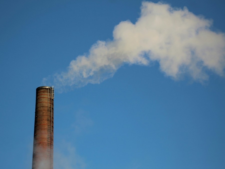 Smoke stack with yellow smoke coming out of the top against a blue sky.