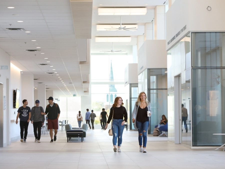Students walking down a large, naturally lit corridor with light coloured walls