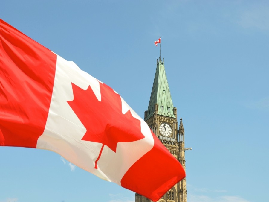 Canadian flag in front of Parliament Hill's Peace Tower against a blue sky..