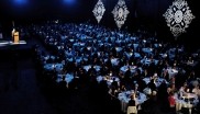 Dark banquet hall with hundreds of guests sitting at round tables